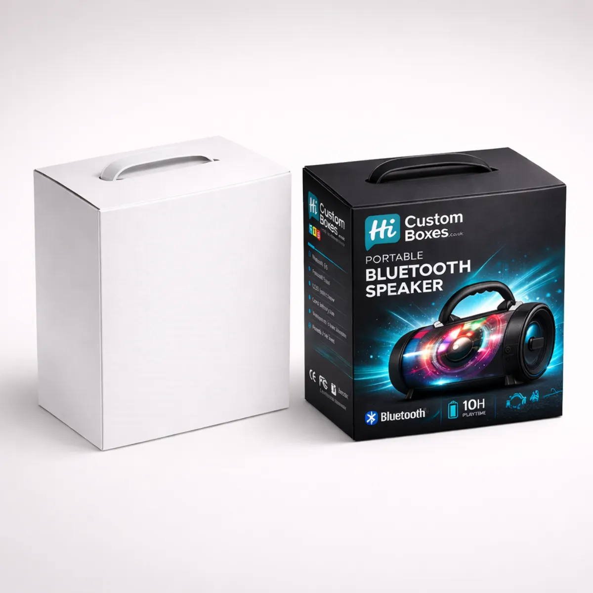 A plain white box next to a black portable speaker box featuring a carry handle. class=